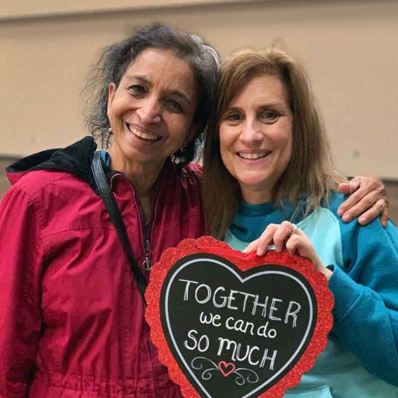 A BAMOW volunteer and her client, smiling together and holding a chalkboard heart that reads 'Together we can do so much'