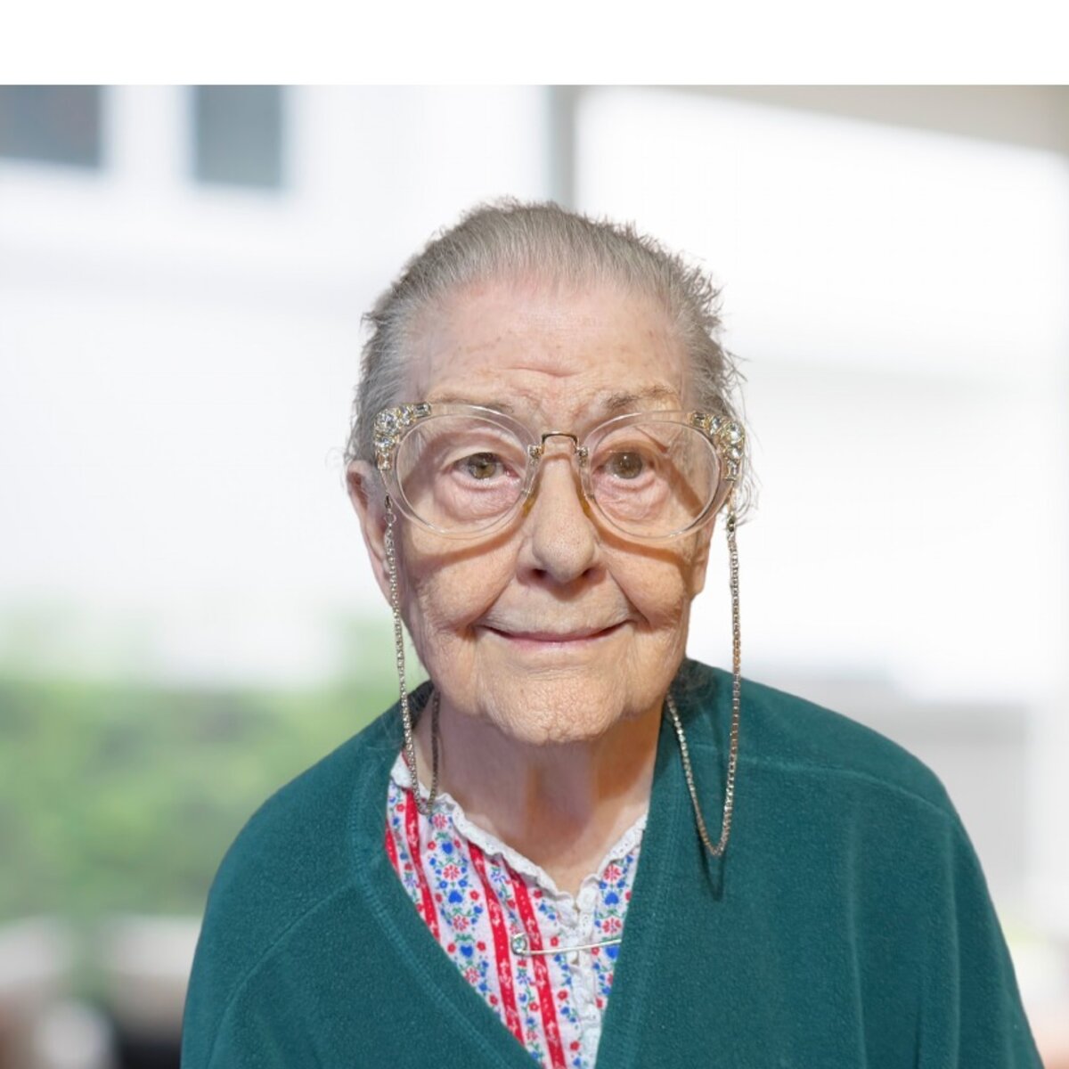 Shirley, a smiling older woman with glasses, in her sunlit living room